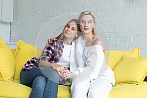 Portrait of beautiful lesbian couple in casual clothes that hugging, sitting on yellow sofa at home
