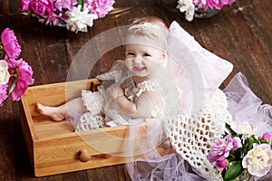 Portrait of a beautiful little baby girl with pink flowers. Sweet smiling girl sitting in wooden box on the floor