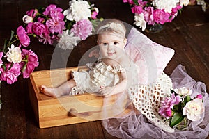 Portrait of a beautiful little baby girl with pink flowers. Sweet smiling girl sitting in wooden box on the floor
