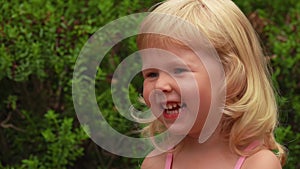 Portrait of a beautiful little blond girl smiling in sunny park outdoors