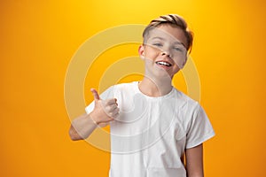 Portrait of beautiful little boy giving you thumbs up over yellow background