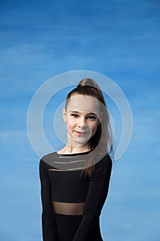 Portrait of a beautiful little brown-haired girl smiling on a blue background. Dressed in a black sweater