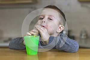 Pretty boy drinks iced tea through a plastic straw in the kitchen