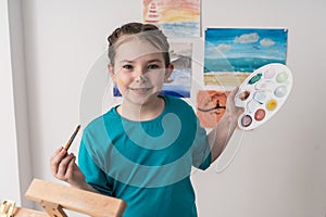 Portrait of a beautiful little girl artist. A pre-adolescent girl paints with a brush and palette.