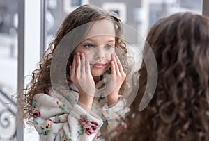 Portrait of beautiful little girl enjoying skincare cleansing procedures front of the mirror in her home bathroom