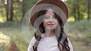 Portrait of beautiful little girl in hat looking at camera and smiling. Happy cute child having fun in park outdoors