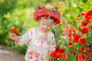 Portrait of a beautiful little girl having fun in field of red poppy flowers in spring.