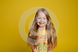 Portrait of beautiful little girl with long hair smiling posing isolated at yellow studio background