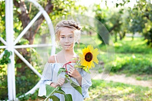 Portrait of beautiful little girl with pigtail on her head holds sunflower. Childhood concept. Teenager girl with sunflower in gar