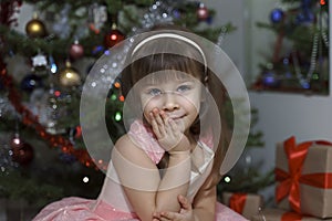 portrait of a beautiful little girl in a pink dress by the christmas tree