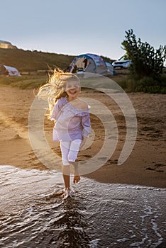 Portrait of beautiful little girl is playing in sea waves in sunset light