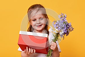Portrait of beautiful little girl with red gift and bouquet of blue florets, preparing for Mother`s Day, wants to congratulate he