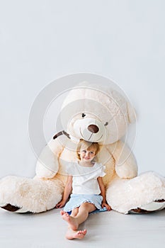 Portrait of the beautiful little girl sitting with a huge teddy bear.