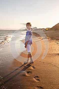 Portrait of beautiful little girl walking in sea waves in sunset light