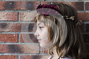 portrait of a beautiful little girl wearing a red wreath roses on her head. Brick background. Lifestyle