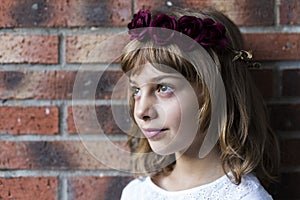 Portrait of a beautiful little girl wearing a red wreath roses on her head. Brick background. Lifestyle