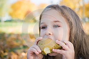 Portrait of a beautiful little girl who eats a pear on a picnic in the autumn park