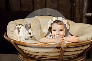 Portrait of a beautiful little girl in a wreath of flowers. A girl with a cute fluffy white Easter bunny