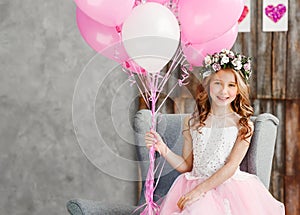 Portrait a beautiful little girl in a wreath of fresh flowers and an elegant pink dress celebrates her birthday in a white studio