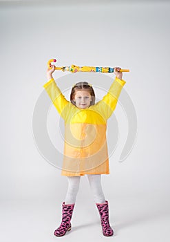 Portrait of a beautiful little girl in a yellow raincoat holding an umbrella in her hands on an isolated white