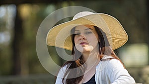 Portrait of beautiful long-haired Hispanic young woman wearing a hat sitting on a park bench with a pensive attitude against a