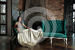 Portrait of beautiful magnificent fashion model woman wearing fashionable silver evening gown posing in vintage palace interior