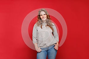 Portrait of beautiful mature brunette woman in grey sweater and blue jeans on red studio wall background