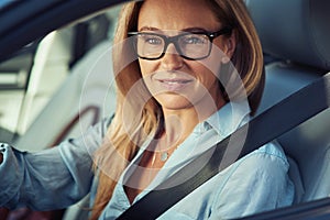 Portrait of a beautiful mature business woman driving a car, sitting behind steering wheel, looking at camera and