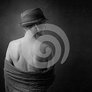 Portrait of a beautiful mature woman with bare shoulders. Attractive slender woman in the hat turned her back