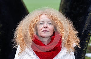 Portrait of a beautiful mature woman in her forties with wild red curls and a white coat stands in a wave of tar partially covered