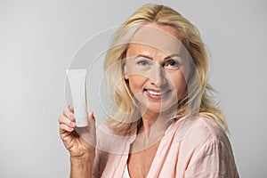 Portrait of beautiful mature woman with perfect skin holding tube of cream