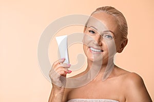 Portrait of beautiful mature woman with perfect skin holding tube of cream on background. Space for text