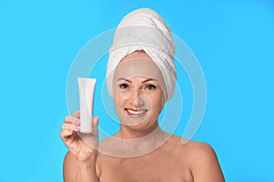 Portrait of beautiful mature woman with perfect skin holding tube of cream on blue background