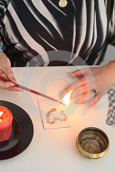 Portrait of beautiful middle age woman sits near a fortune teller desk with a tarot cards, black pendulum and candles.