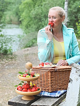 Portrait of a beautiful middle-aged caucasian blonde woman eating a big red and ripe strawberry