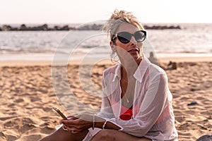 Portrait of beautiful middle aged woman relaxing using phone sitting at the beach