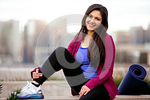 Portrait of a beautiful mixed ethnicity brunette woman in sportswear, sitting relaxed after a morning yoga workout with city skyli