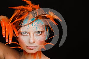 Portrait of a beautiful model with creative make-up and hairstyle using orange feathers