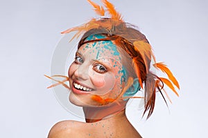 Portrait of a beautiful model with creative make-up and hairstyle using orange feathers