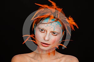 Portrait of a beautiful model with creative make-up and hairstyle using orange feathers