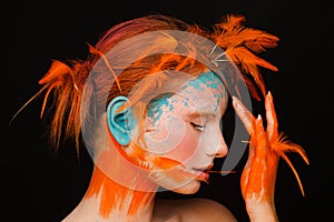 Portrait of a beautiful model with creative make-up and hairstyle using orange feathers