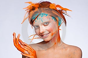 Portrait of a beautiful model with creative make-up and hairstyle using orange feathers