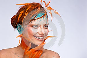 Portrait of a beautiful model with creative make-up and hairstyle using orange feathers