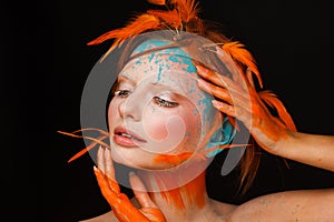 Portrait of a beautiful model with creative make-up and hairstyle using orange feathers