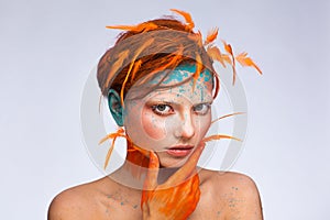 Portrait of a beautiful model with creative make-up and hairstyle using orange feathers