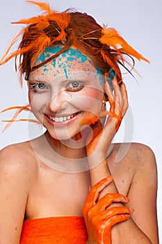 Portrait of a beautiful model with creative make-up and hairstyle using orange feathers