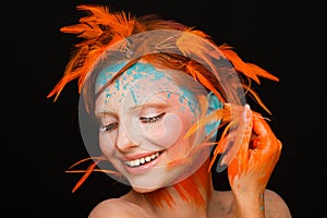 Portrait of a beautiful model with creative make-up and hairstyle using orange feathers