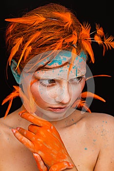 Portrait of a beautiful model with creative make-up and hairstyle using orange feathers