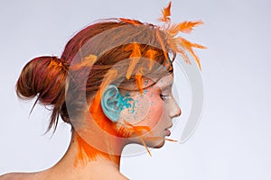 Portrait of a beautiful model with creative make-up and hairstyle using orange feathers