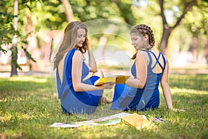 Portrait of a beautiful, modern and young girls in modern dresses in a park. Fashionable and charming young girls with books.